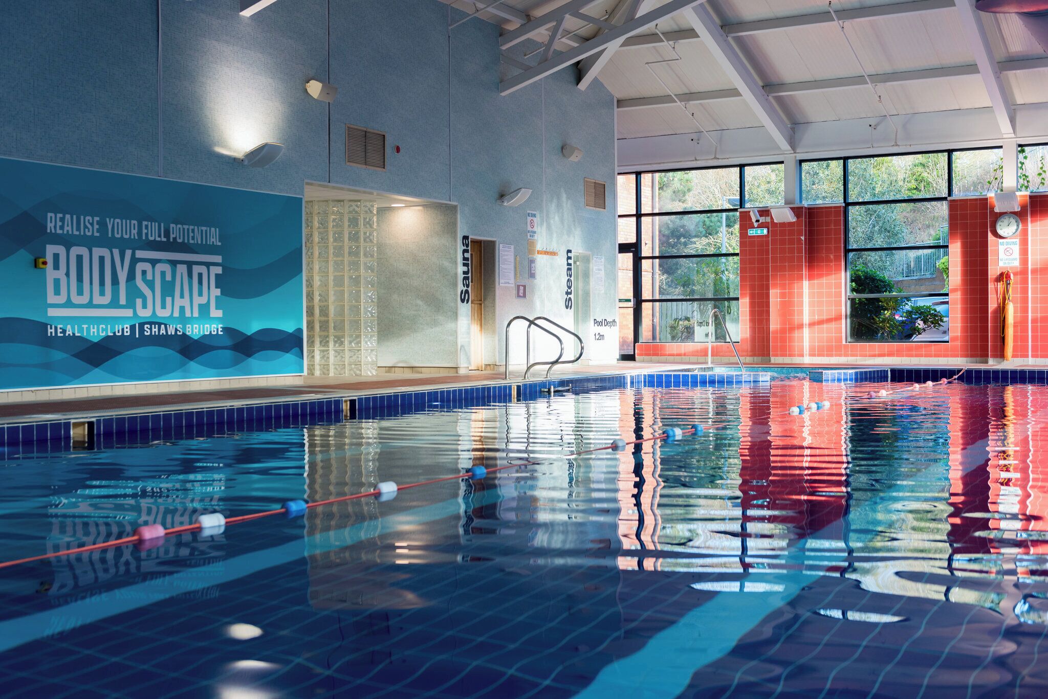 Una piscina interior con señalización clara para diferentes instalaciones, como sauna y salas de vapor, e indicador de profundidad.