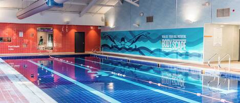 Una piscina interior con marcas de carriles bien definidas, un indicador de profundidad que señala 1,2 metros y un mural publicitario que anuncia 'BODYSCAPE'.