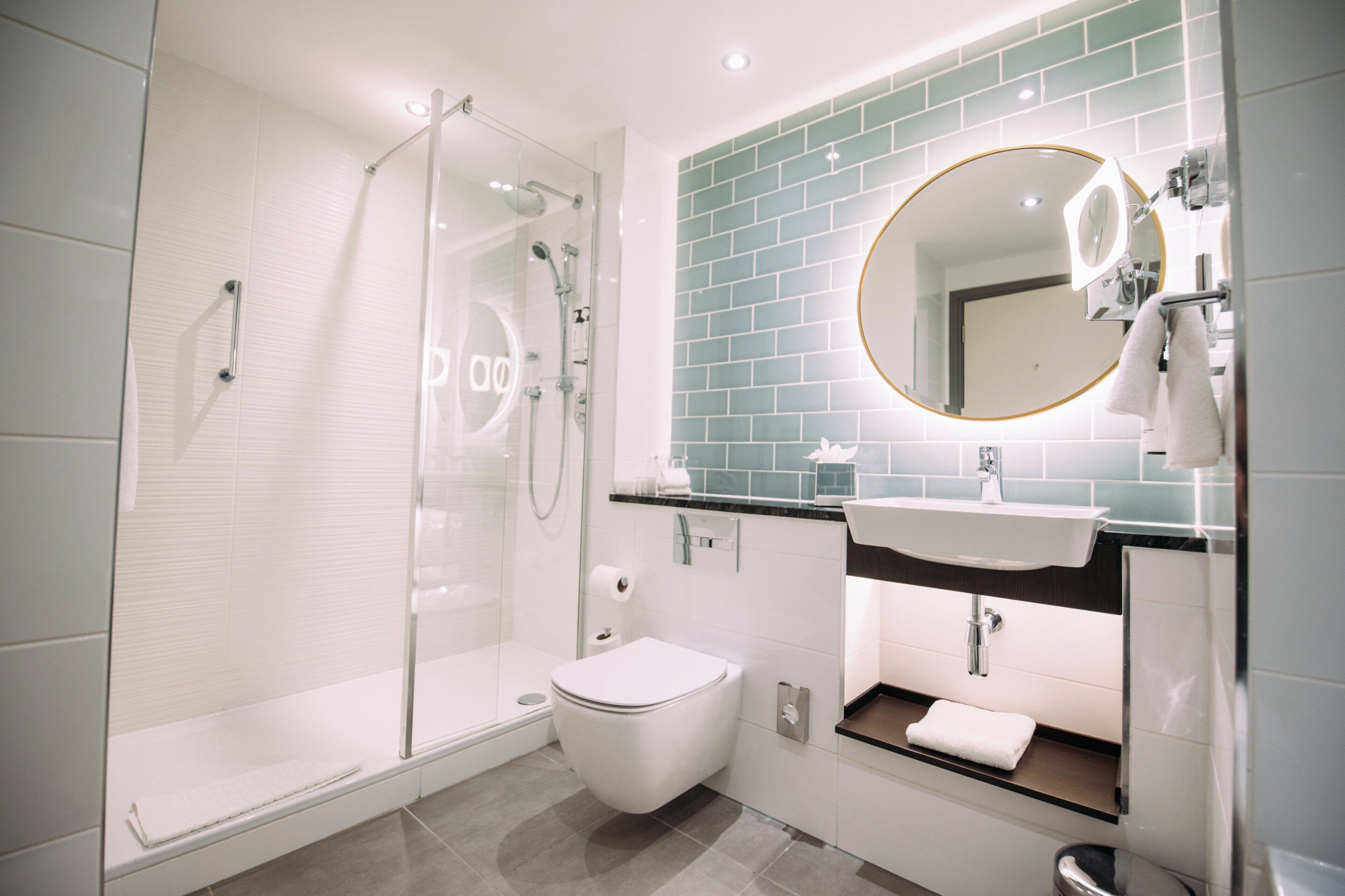 A modern bathroom with a glass-enclosed shower, a white toilet, and a sink with a mirror above it.