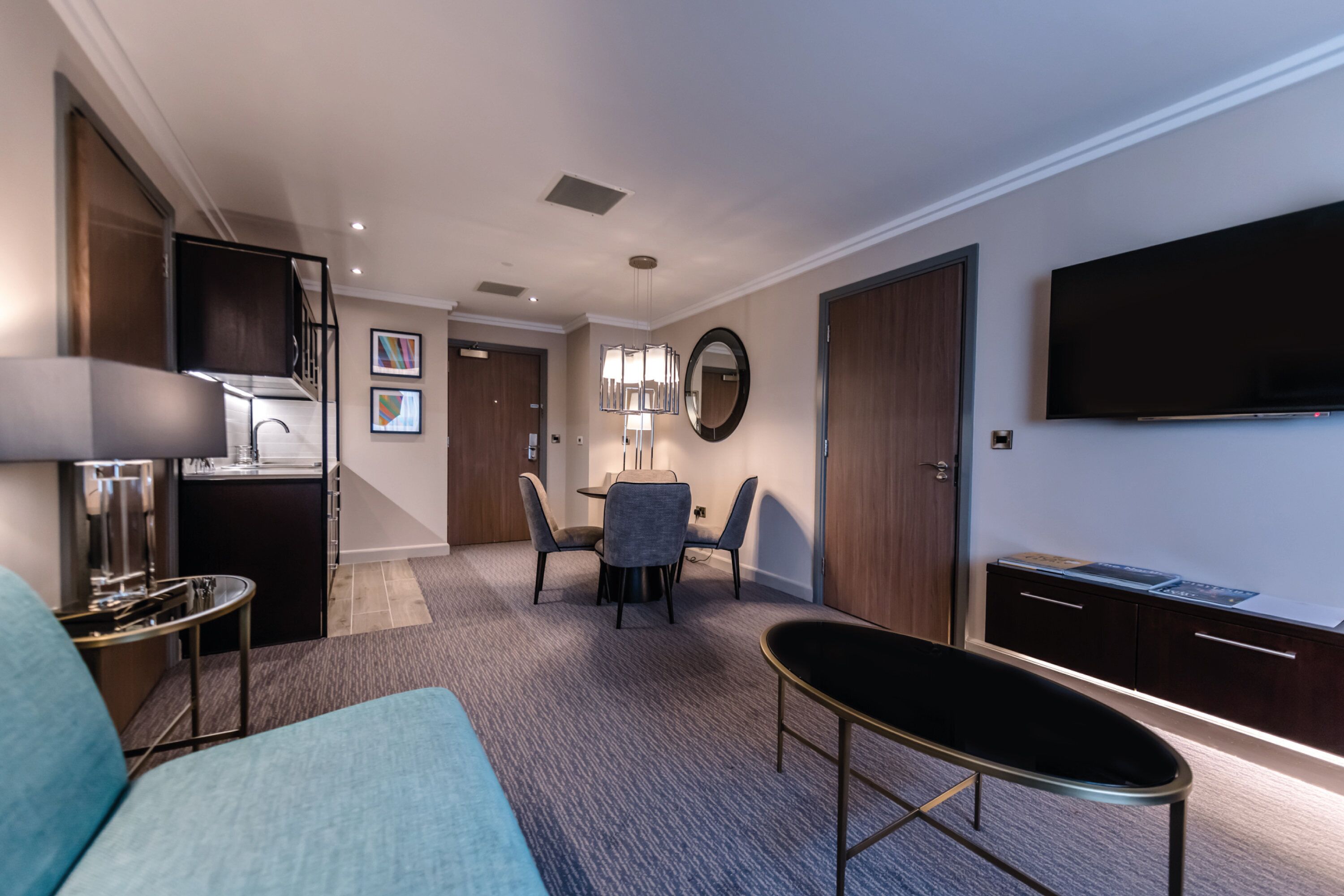 Une chambre d’hôtel moderne équipée d’un canapé, d’une table à manger avec des chaises, d’une télévision et d’un bureau avec des tiroirs.