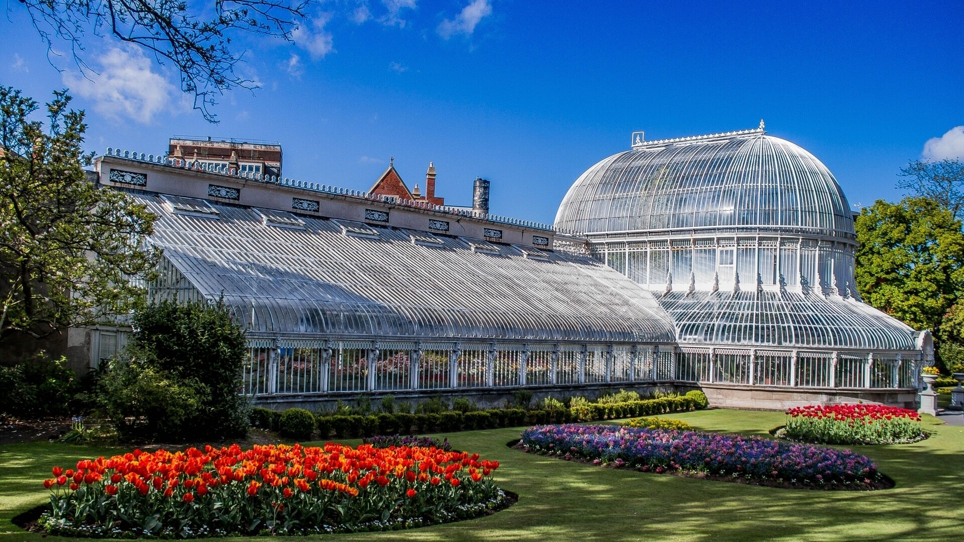 A large greenhouse with a glass dome, surrounded by well-maintained flower beds.
