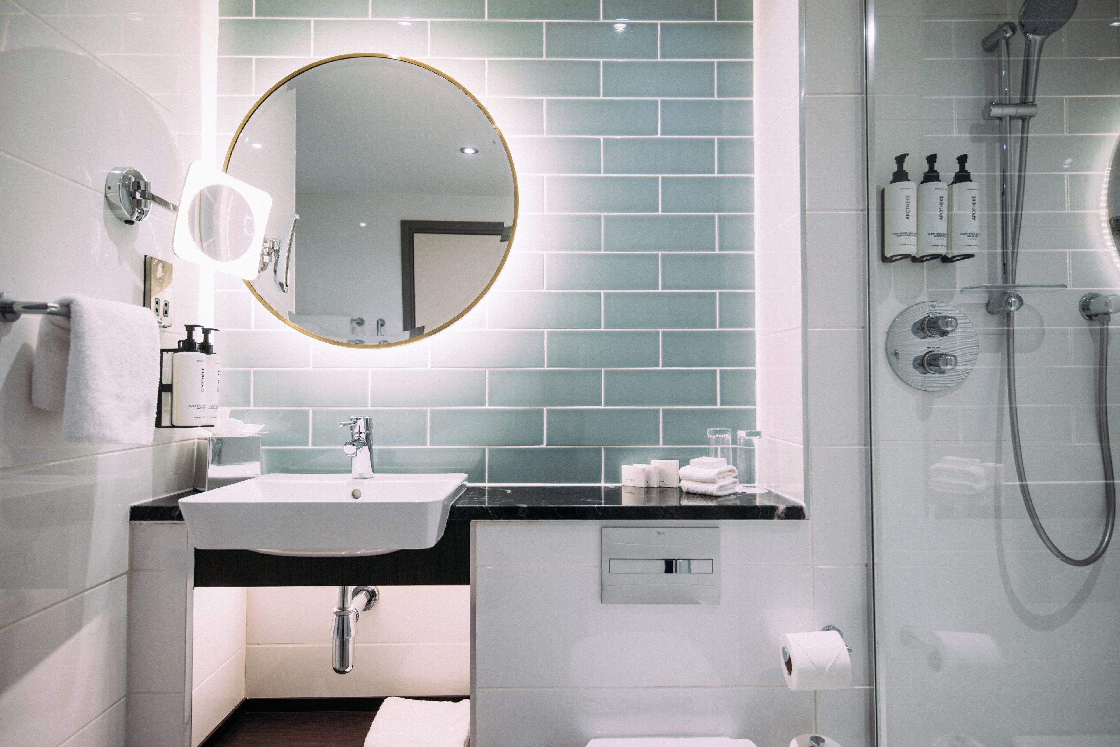 Een moderne badkamer met een ronde spiegel, een wit wastafelmeubel en een douchecabine van glas.