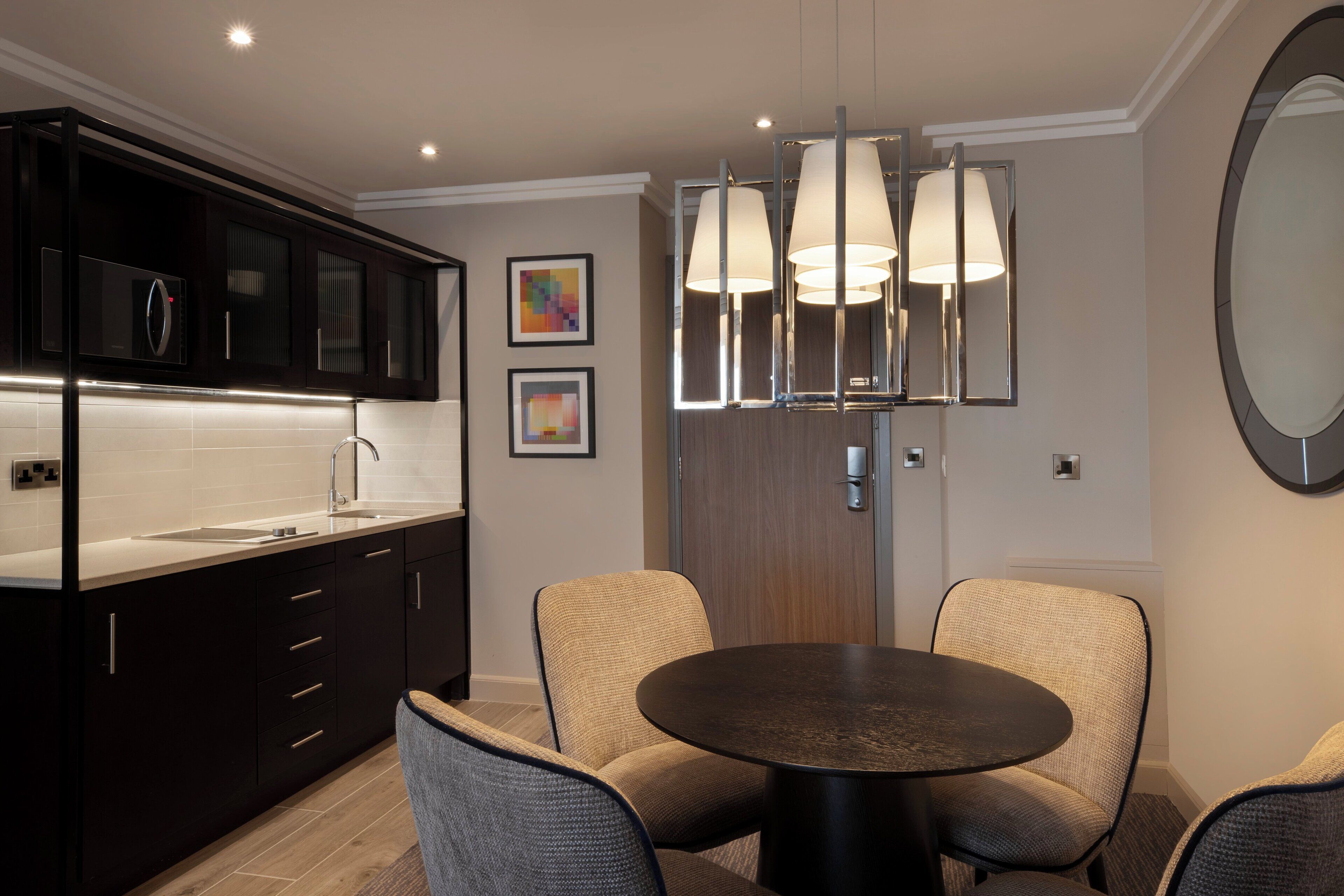 A modern kitchen with dark cabinetry, a round dining table, and a chandelier.