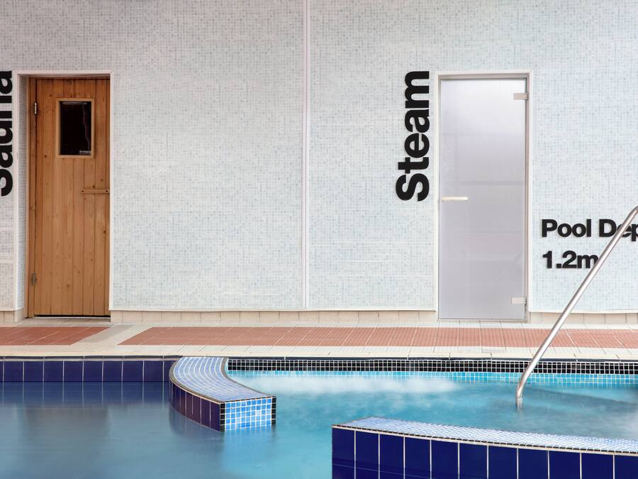 An indoor swimming pool with a wooden sauna door and a steam room door.