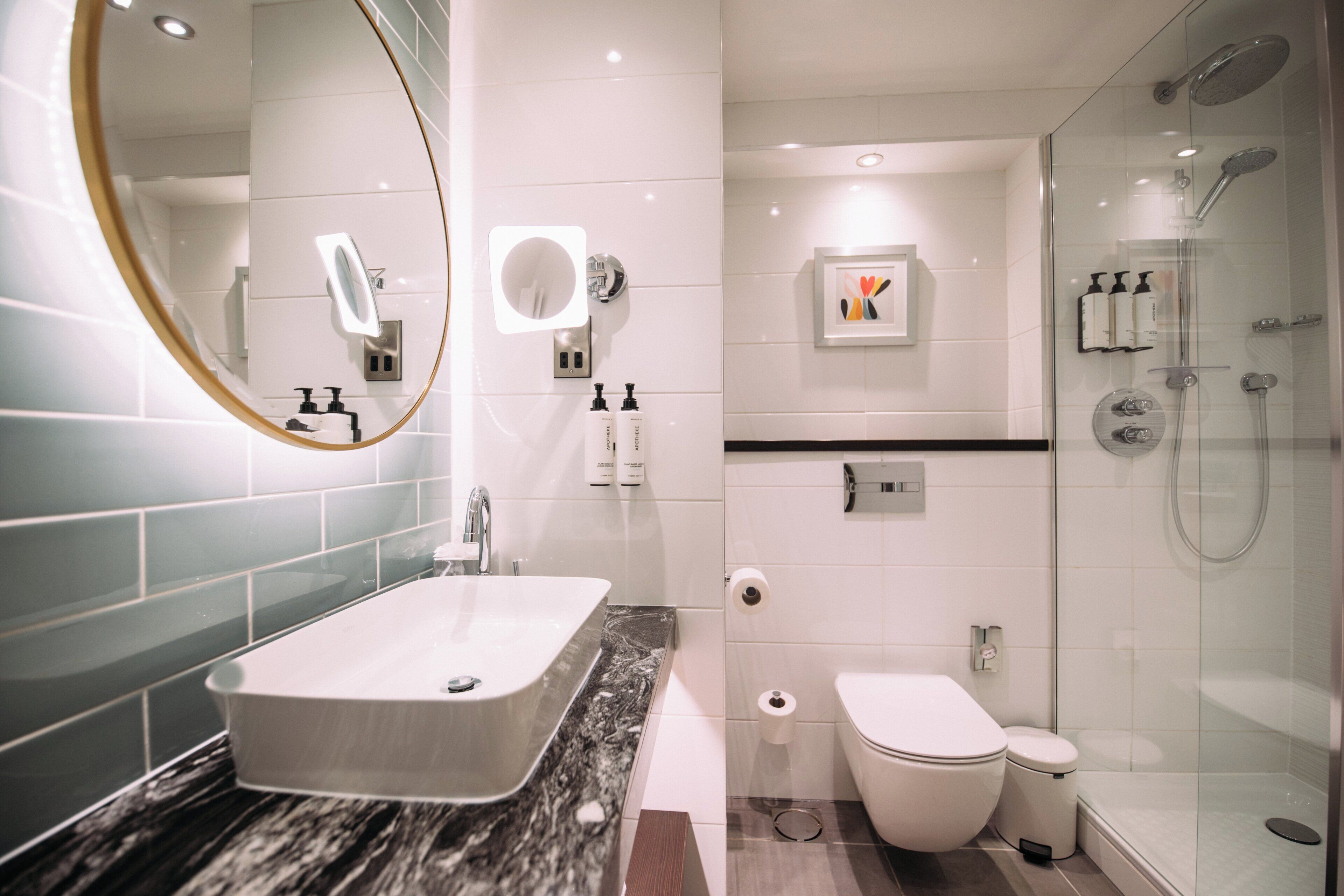 A modern bathroom with a large oval mirror, a rectangular sink, a toilet, and a glass-enclosed shower area.