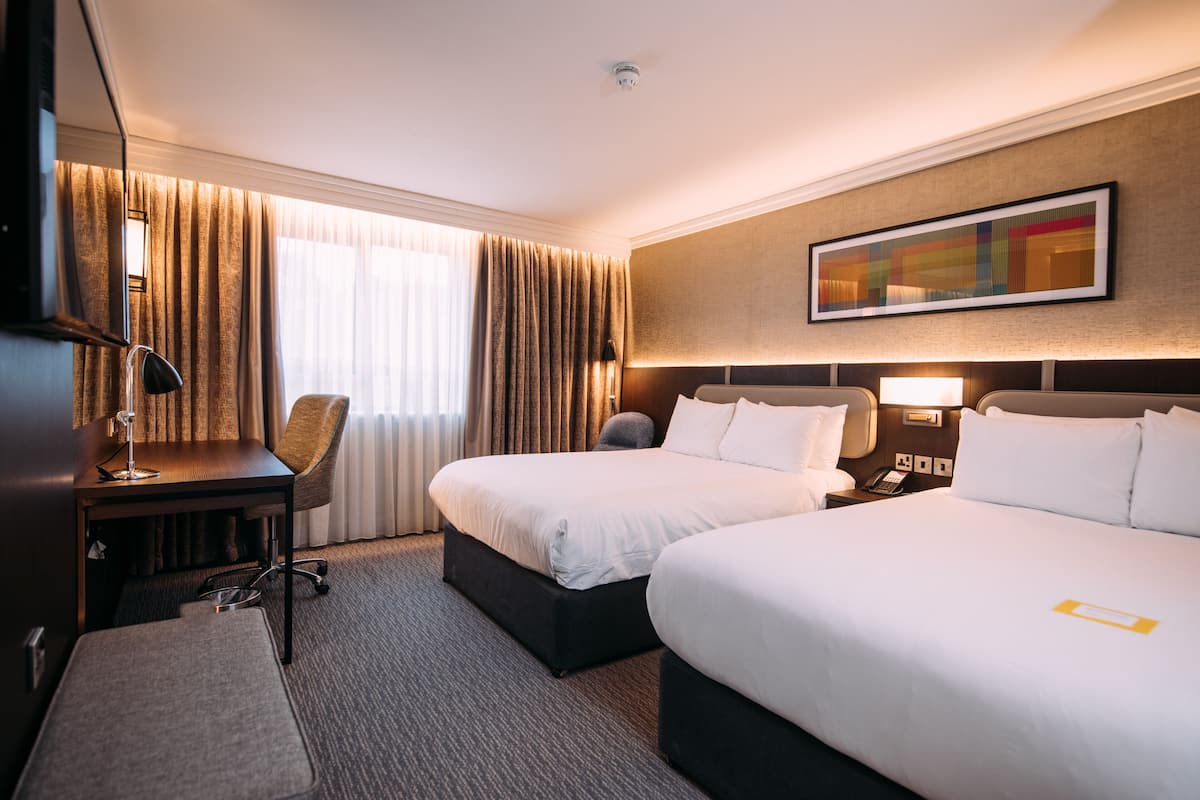 Ett hotellrum med två sängar, ett skrivbord, en stol, en tv och en tavla på väggen.