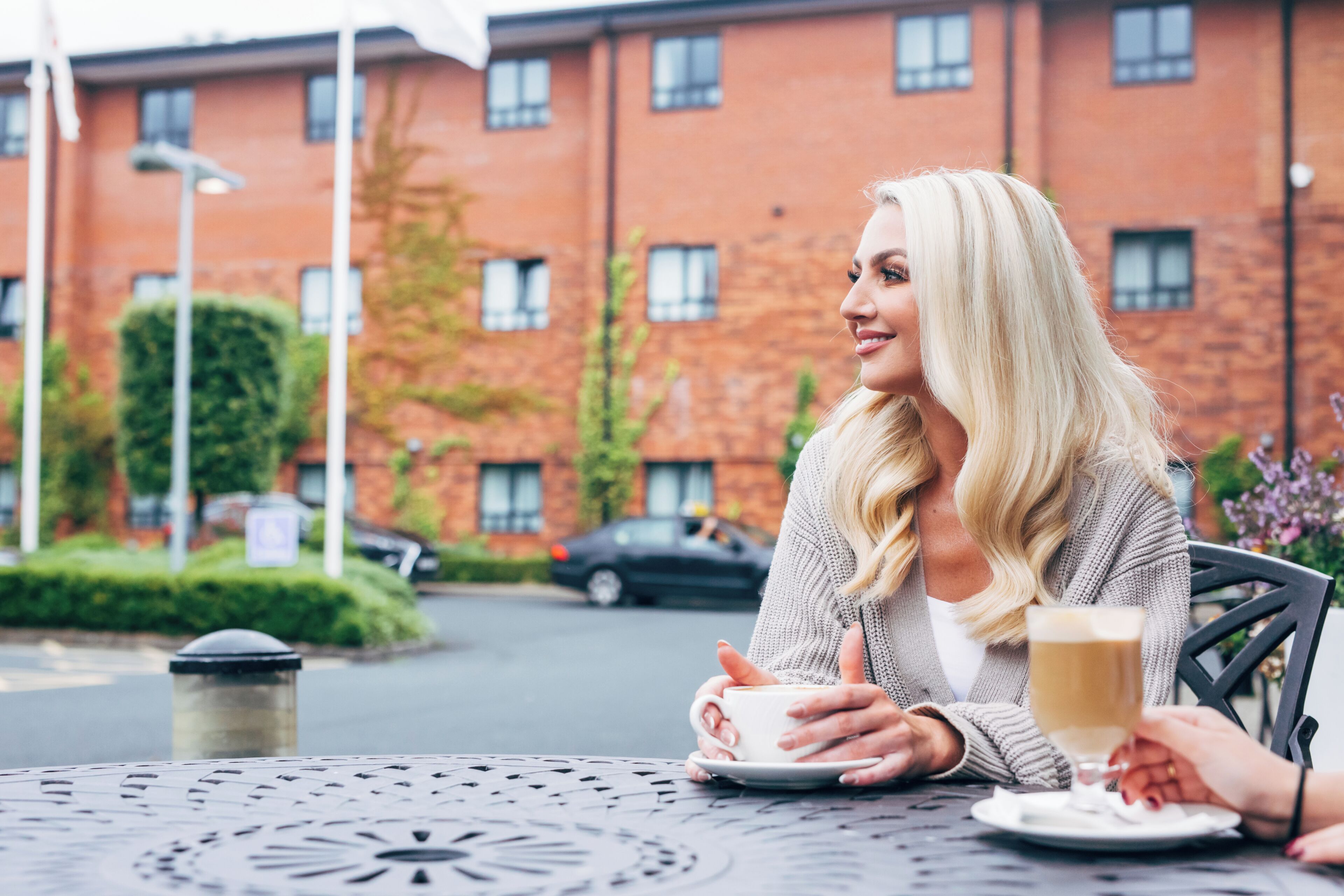 A person sitting at an outdoor table with a cup of coffee, a plate, and a glass of water.