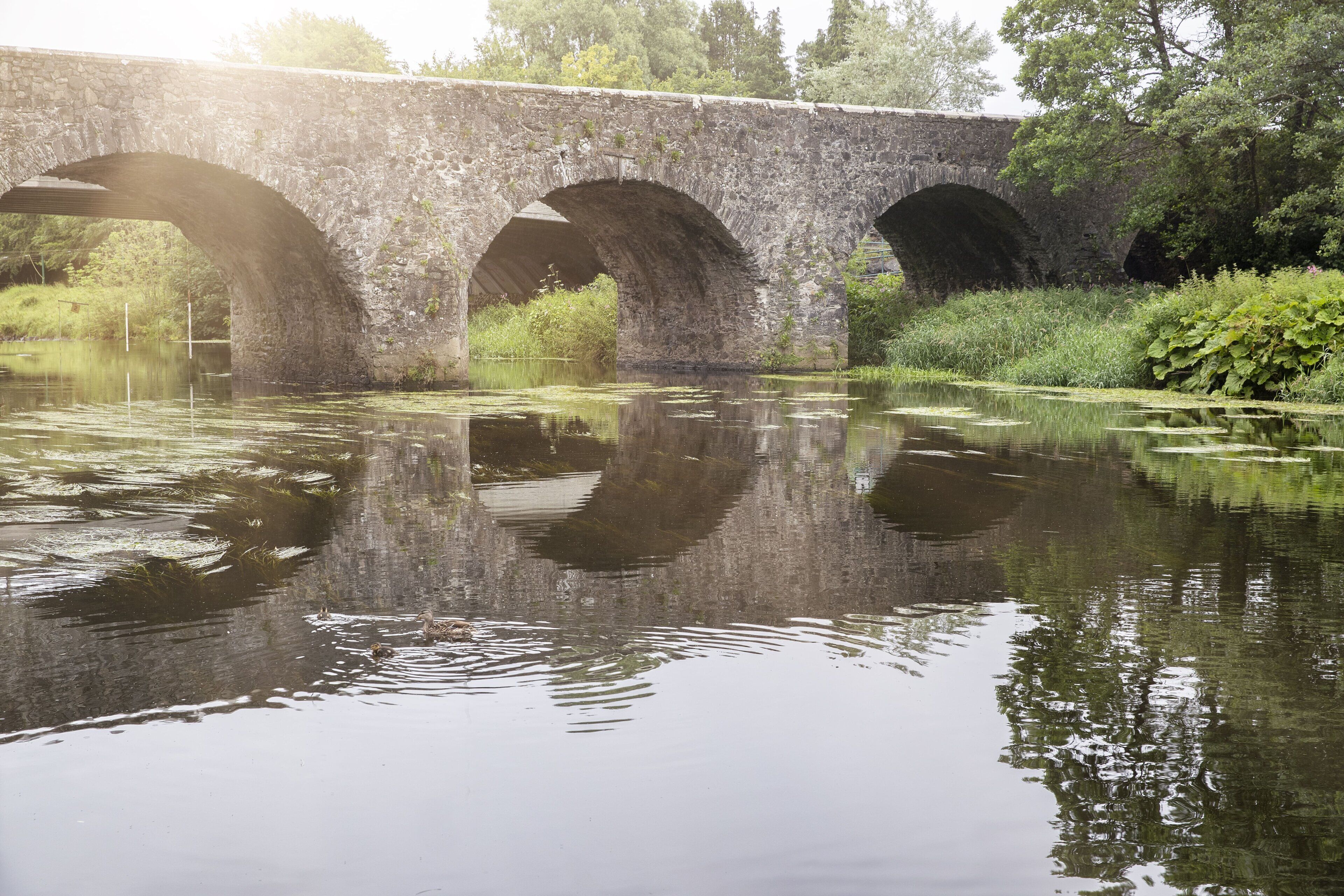 Un puente de piedra sobre un río tranquilo con reflejos.