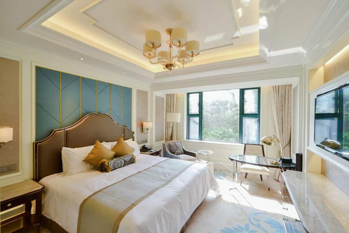 A hotel room with a large bed, a desk, a chair, and a view of the outdoors.