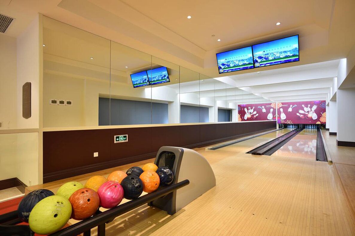 A bowling alley with multiple lanes, a seating area with a mirrored wall, and a row of bowling balls at the end of the lanes.