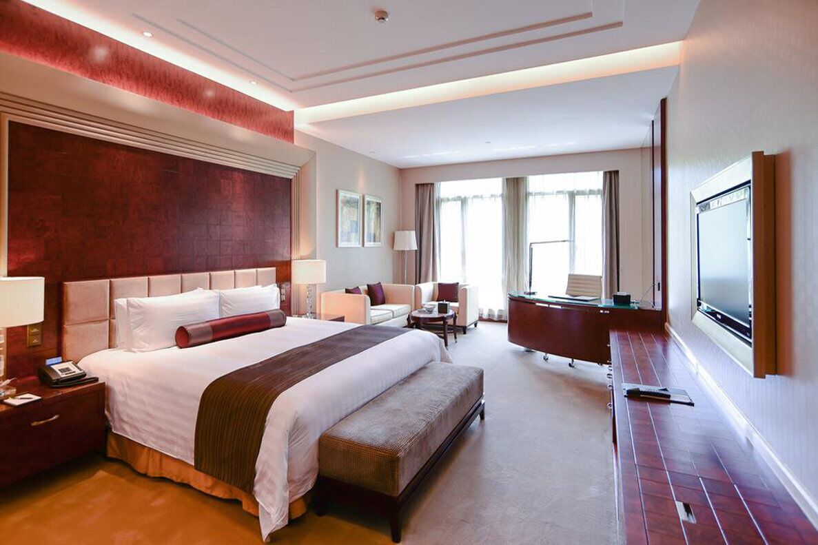 A spacious hotel room with a large bed, a flat-screen TV, a desk, and a comfortable seating area.