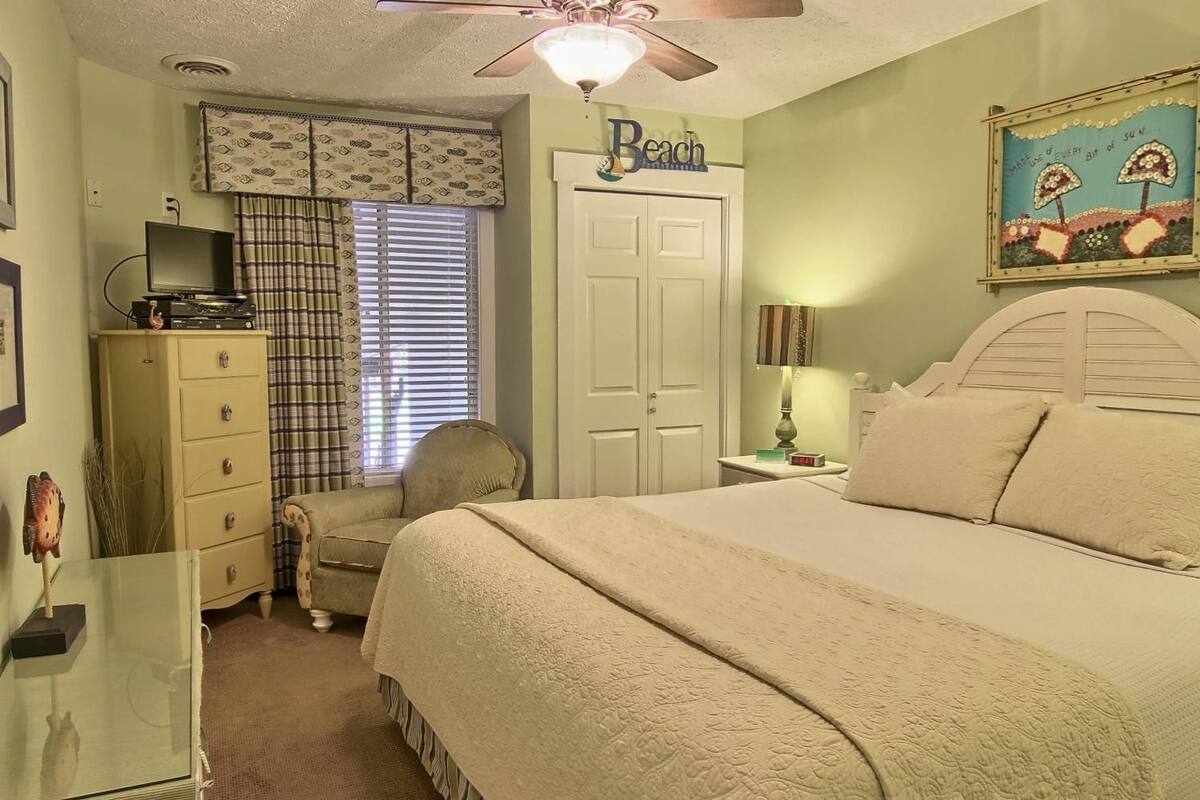 A bedroom with a bed, a chair, a dresser, a ceiling fan, and a window with blinds.