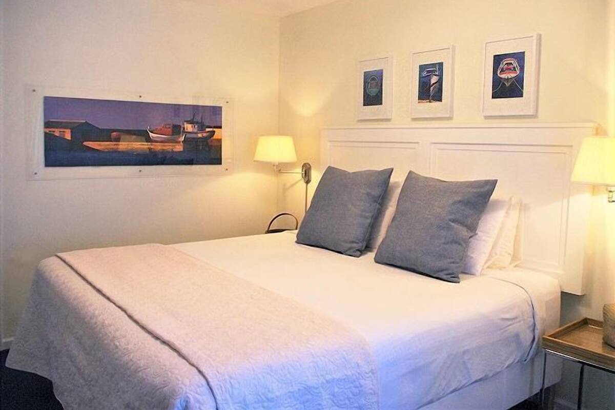 A hotel room with a bed, two bedside lamps, a nightstand, and three framed pictures on the wall.