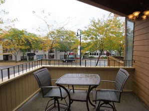 An outdoor patio with a table and chairs, a railing, and a view of the street and trees.