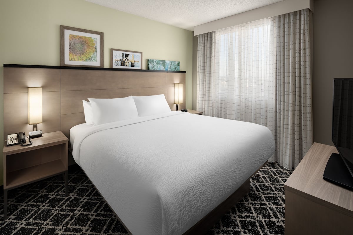 A hotel room with a large bed, two bedside lamps, a flat-screen TV, and artwork on the wall.