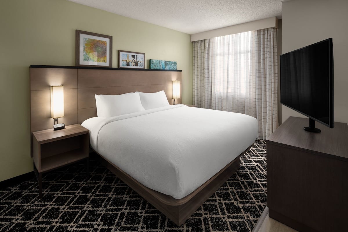 A hotel room with a large bed, bedside lamps, a flat-screen TV, and artwork on the headboard.