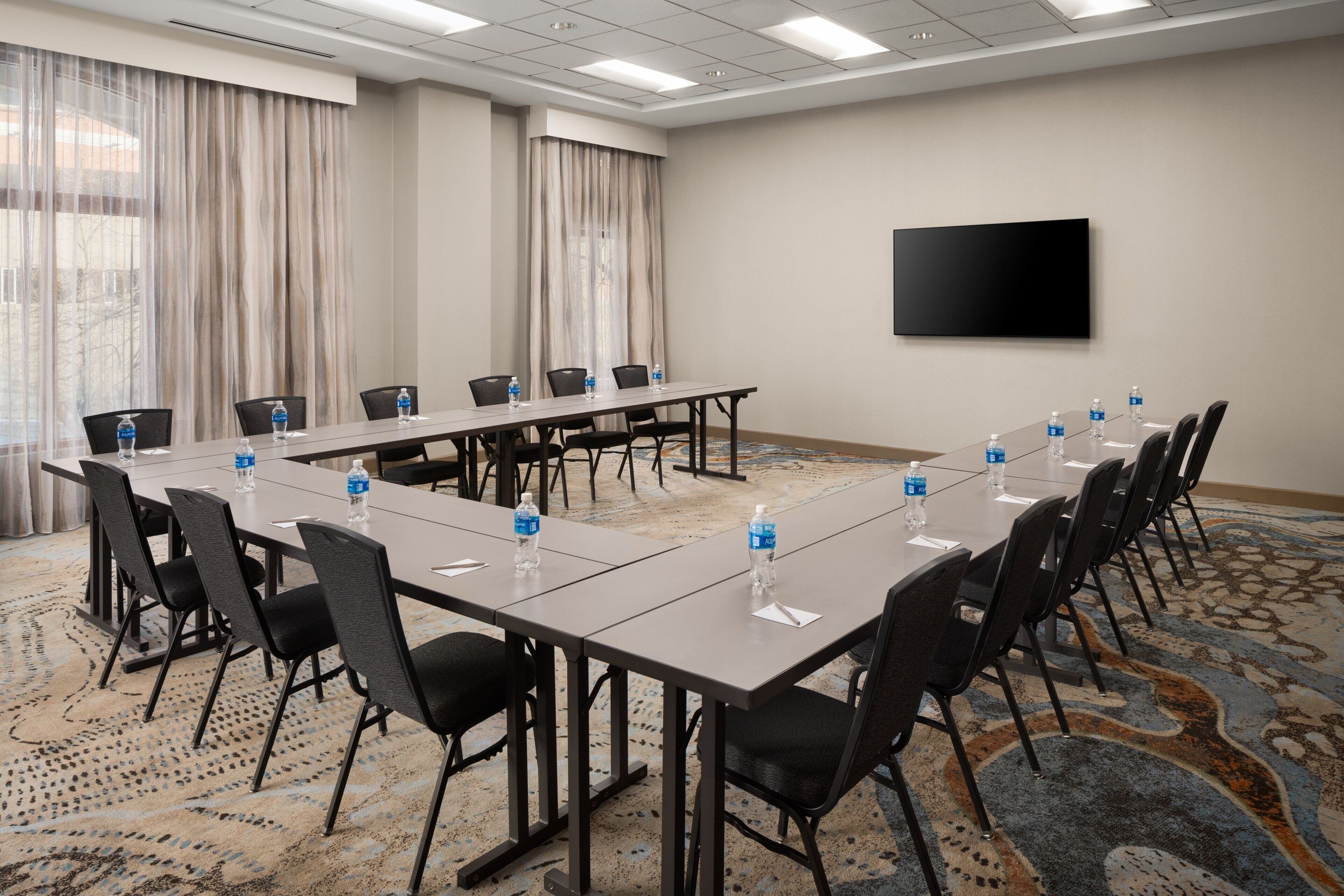 A conference room with a long table, chairs, and a flat-screen TV on the wall.