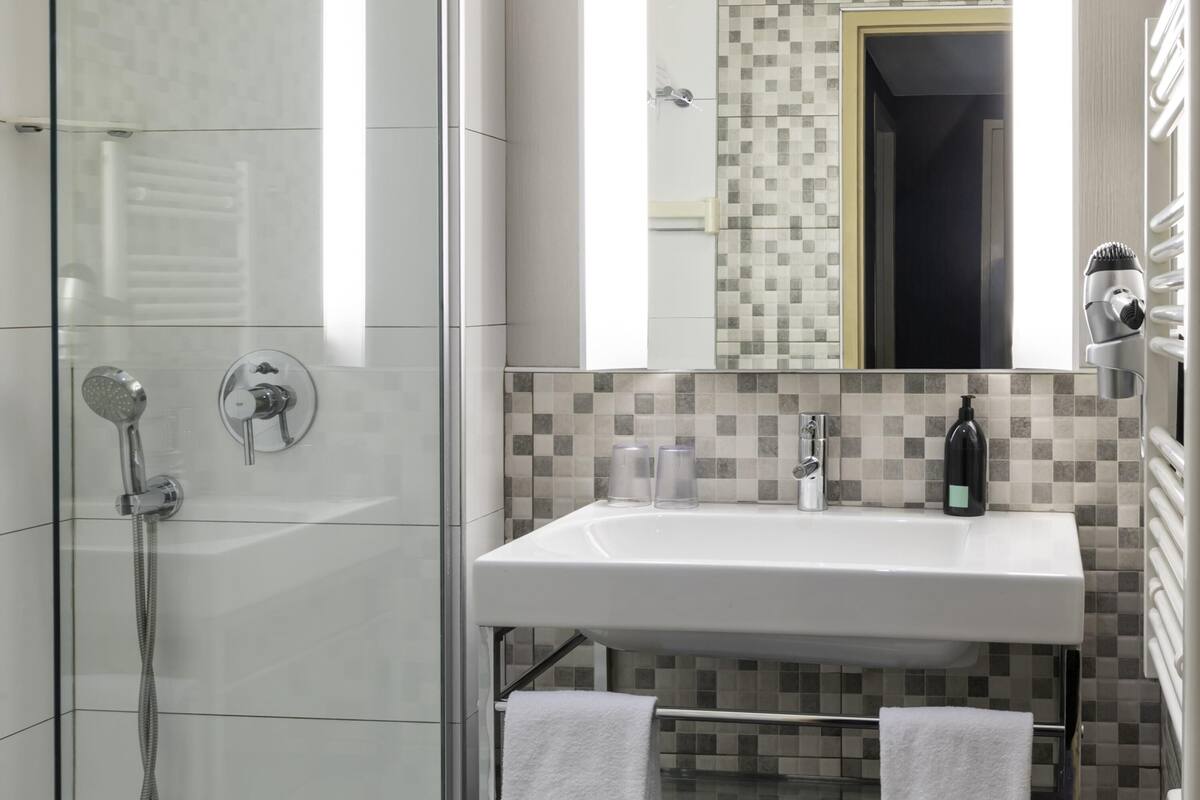 Une salle de bain moderne avec une douche à parois de verre, un lavabo blanc, un miroir et un porte-serviettes.