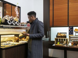 Ein Bereich mit Buffet und vielfältigen Speisen, eine Person bedient, und ein Schild weist auf eine Bar und Gourmet-Desserts hin.