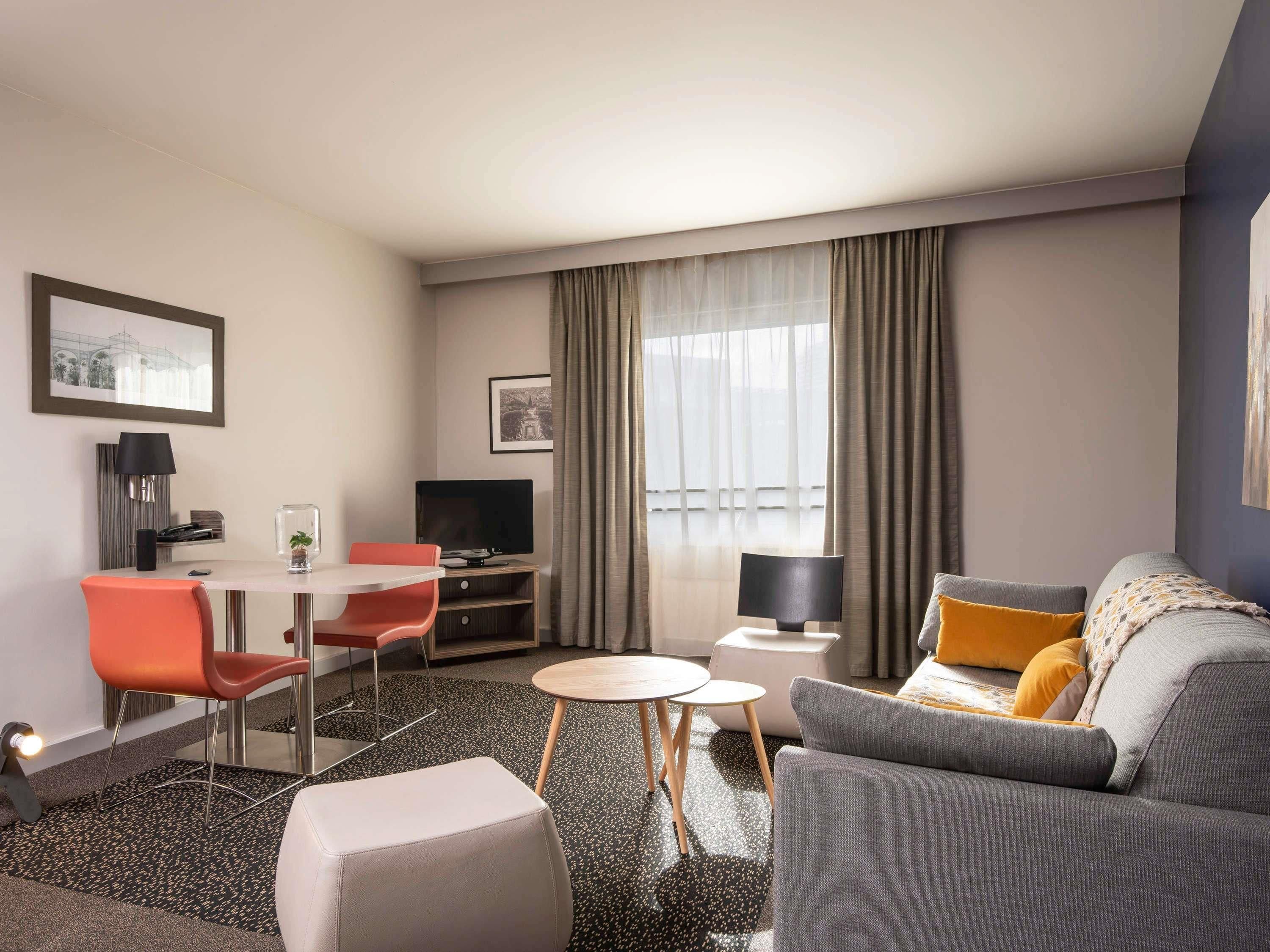 Moderni hotellihuone, jossa on ruokailutila, sohva ja televisio.