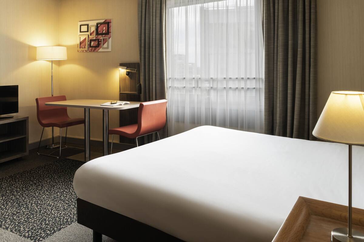 Une chambre d’hôtel avec un lit, un bureau, deux chaises, une télévision et une lampe.