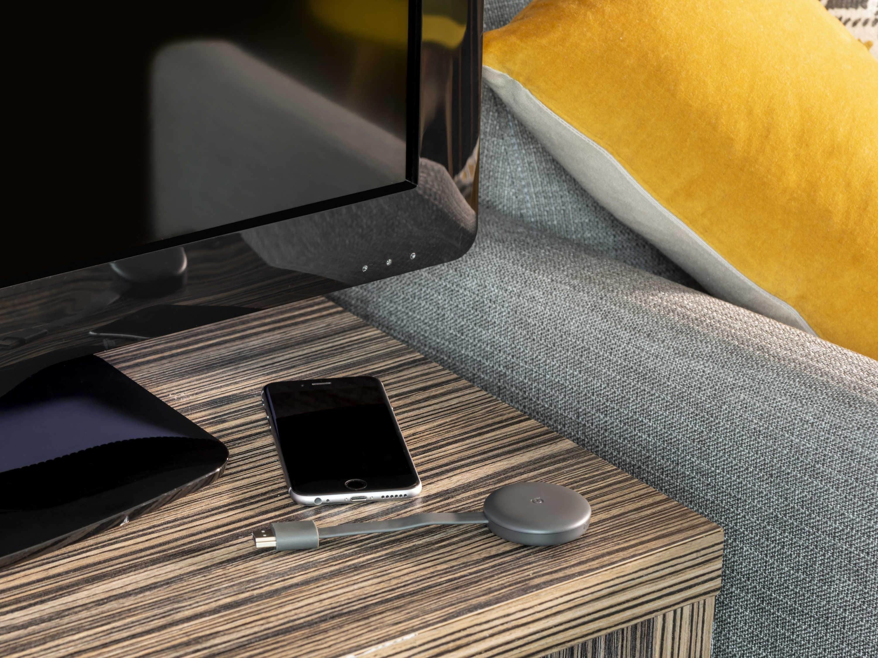 A smartphone, a wired charger, and a wireless charging pad on a wooden side table.