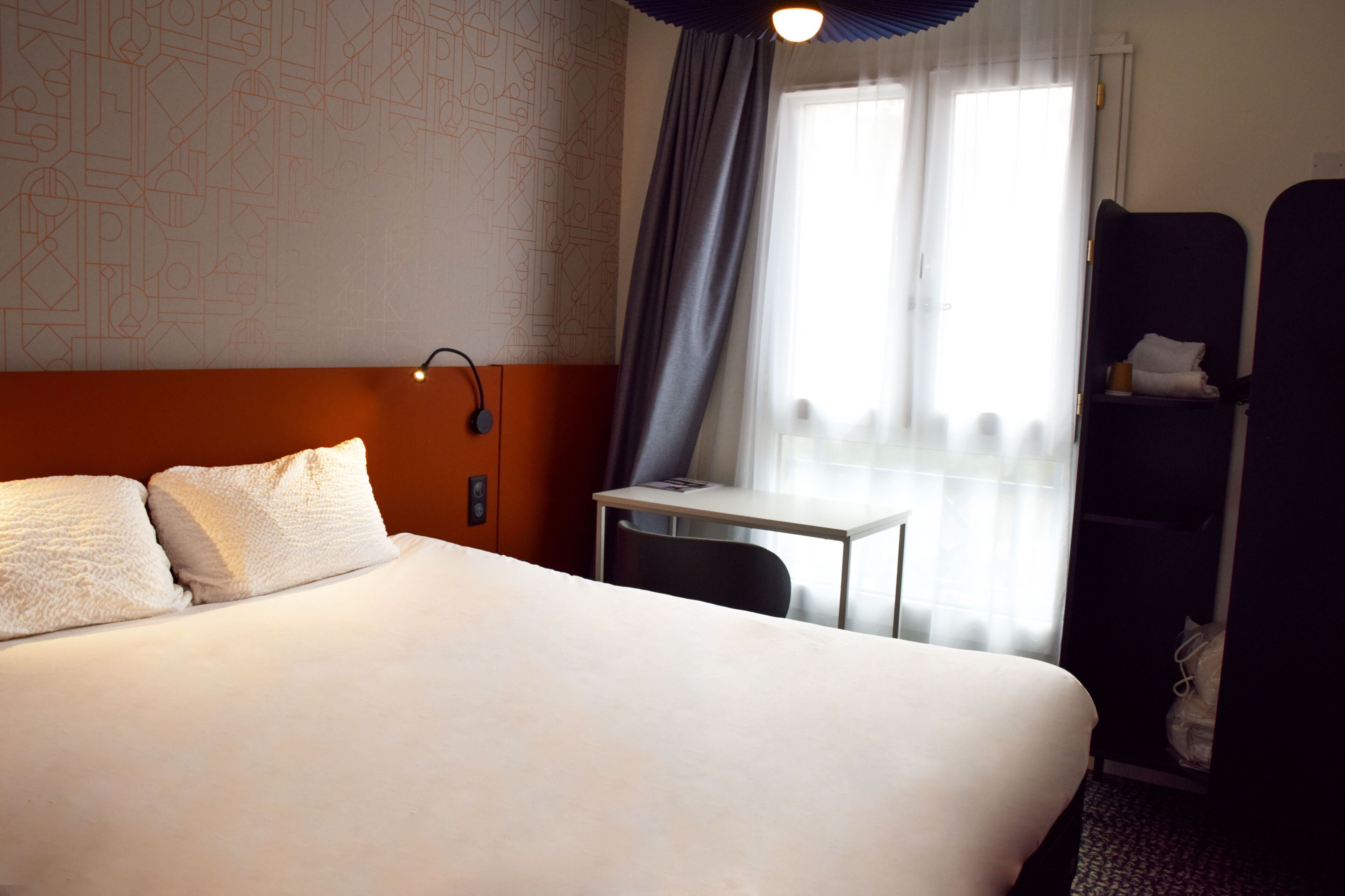 Une chambre d’hôtel avec un grand lit, un bureau, une chaise, une armoire et une fenêtre avec des rideaux.