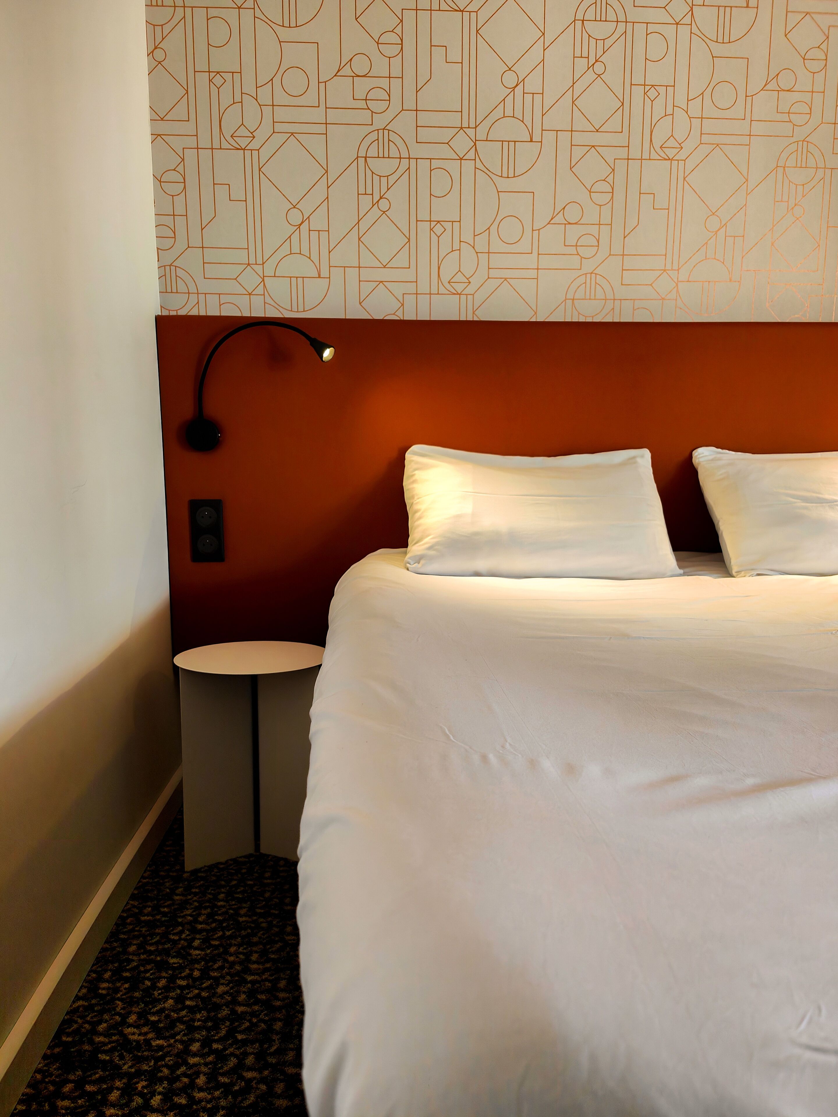 Habitació d'hotel amb un llit, una taula de nit, una làmpada i un mur amb un disseny decoratiu.