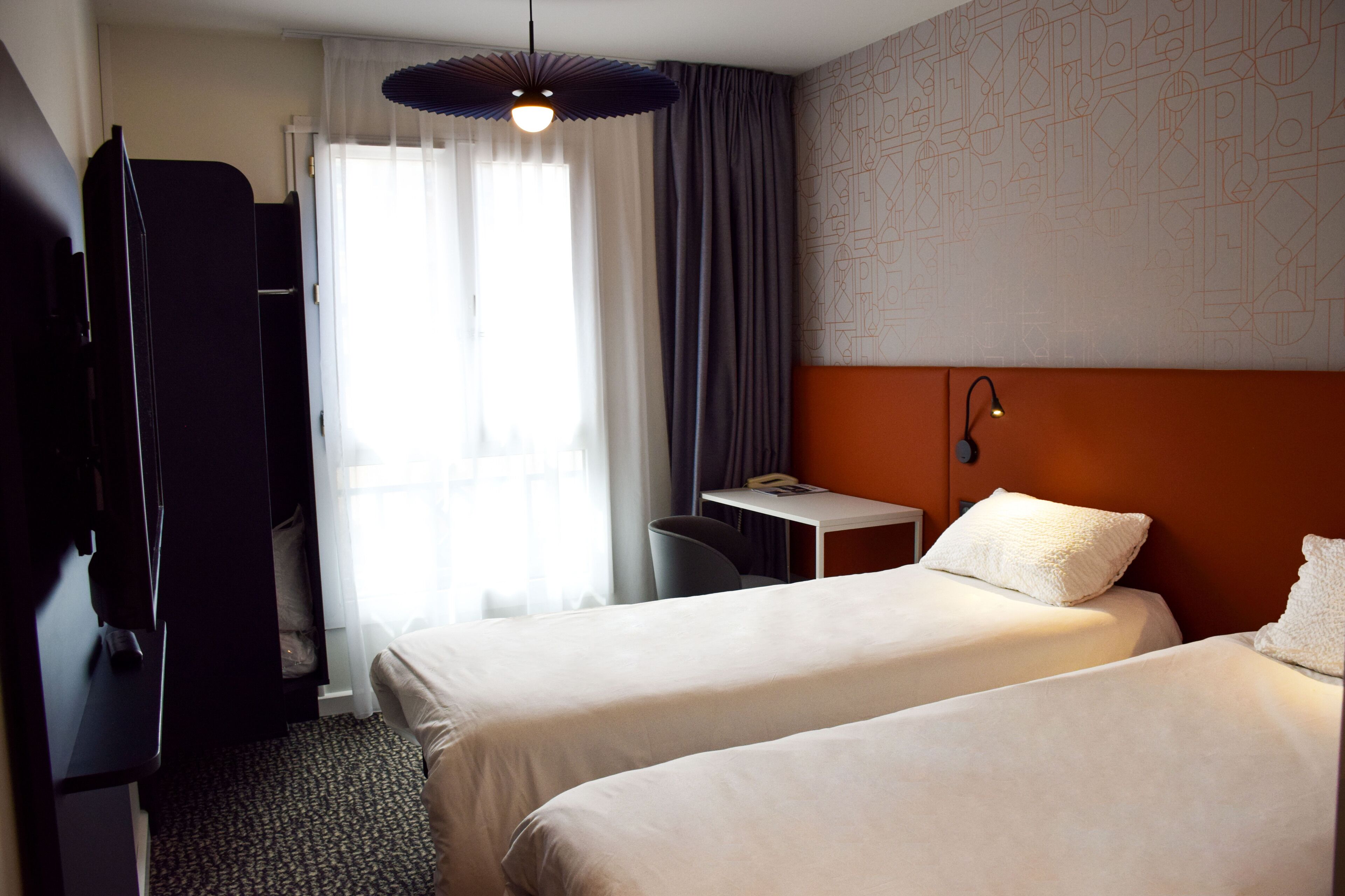 A hotel room with two beds, a desk, a chair, and a TV.