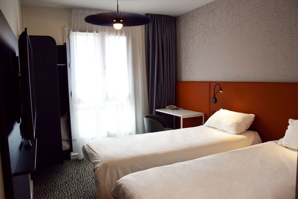 A hotel room with two beds, a desk, a chair, and a TV.