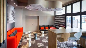 A modern lounge area with a red sofa, black and orange seating, a wooden table, and a patterned carpet. - ibis Rodez Centre Cathédrale (Rodez)