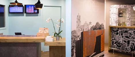 A reception area with a wooden desk, two pendant lights, a wall-mounted TV, and a mural with abstract designs.