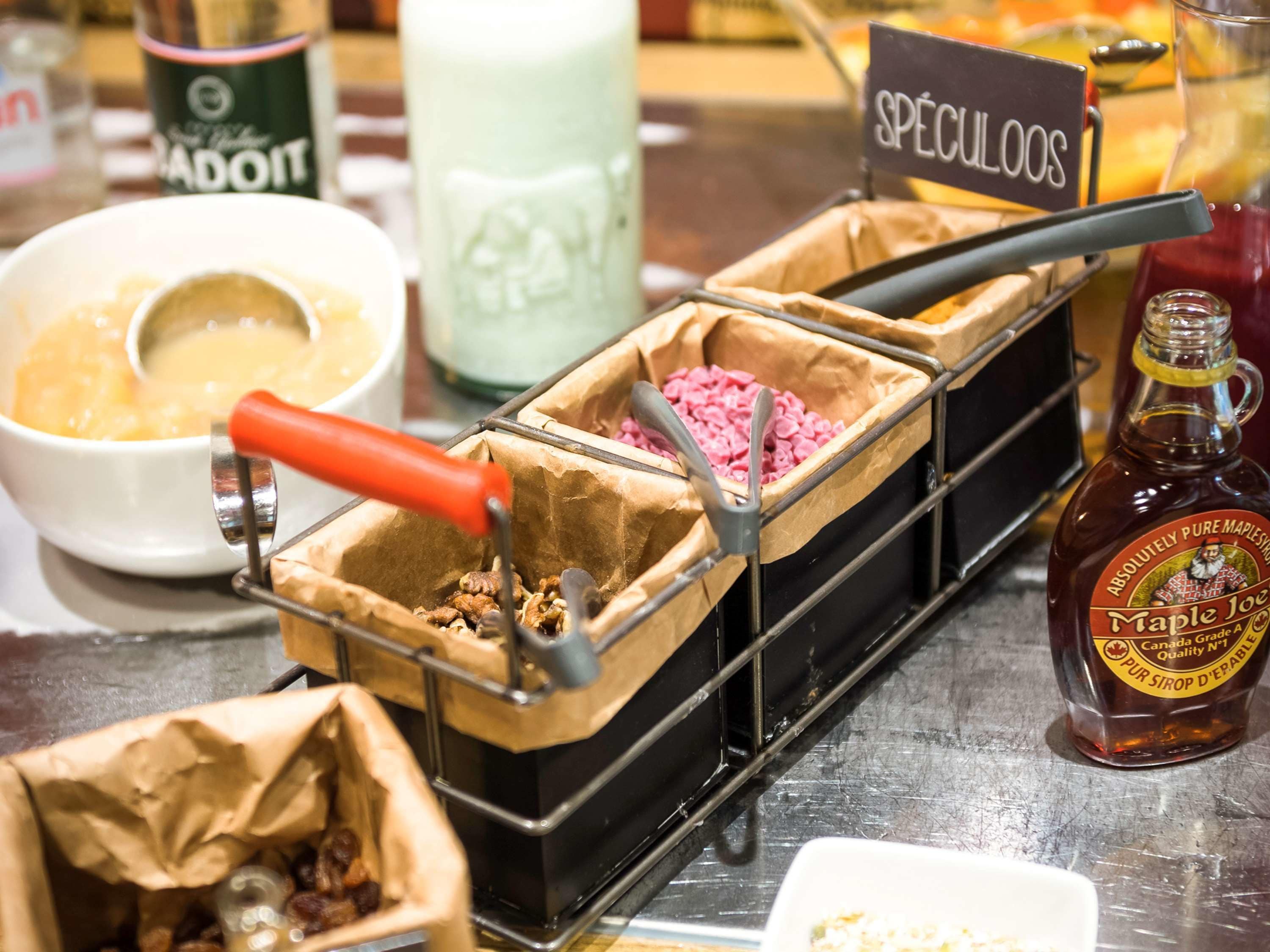 A food display with various items in paper containers, a bottle of maple syrup, and a sign labeled "SPÉCULOOS".