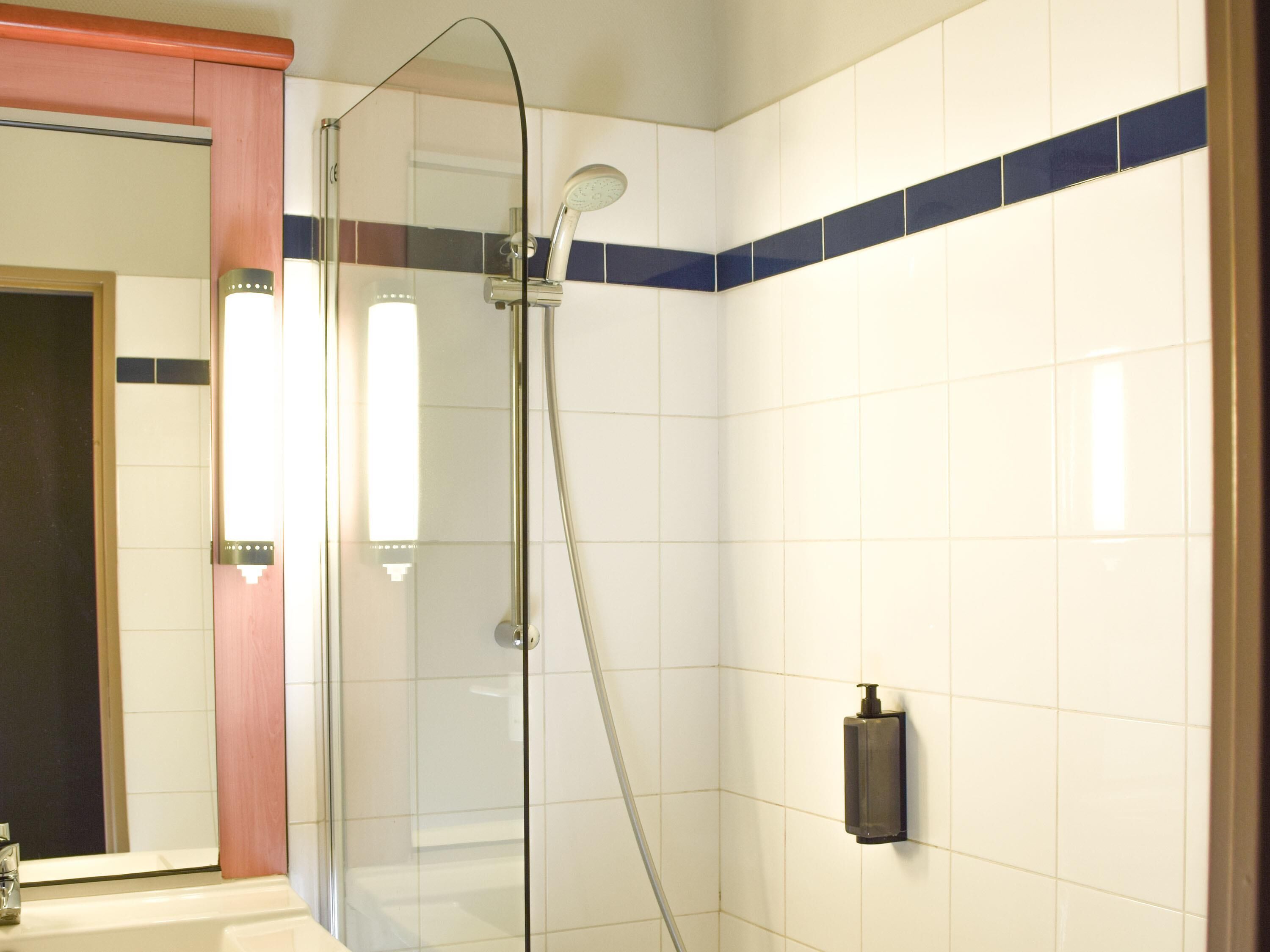 A bathroom with a glass shower enclosure, white tiled walls, and a wooden door frame.