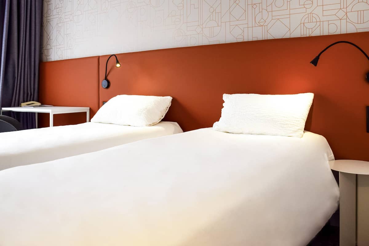 Hotellihuone, jossa on kaksi sänkyä, työpöytä, lamppu ja kuviollinen seinä.