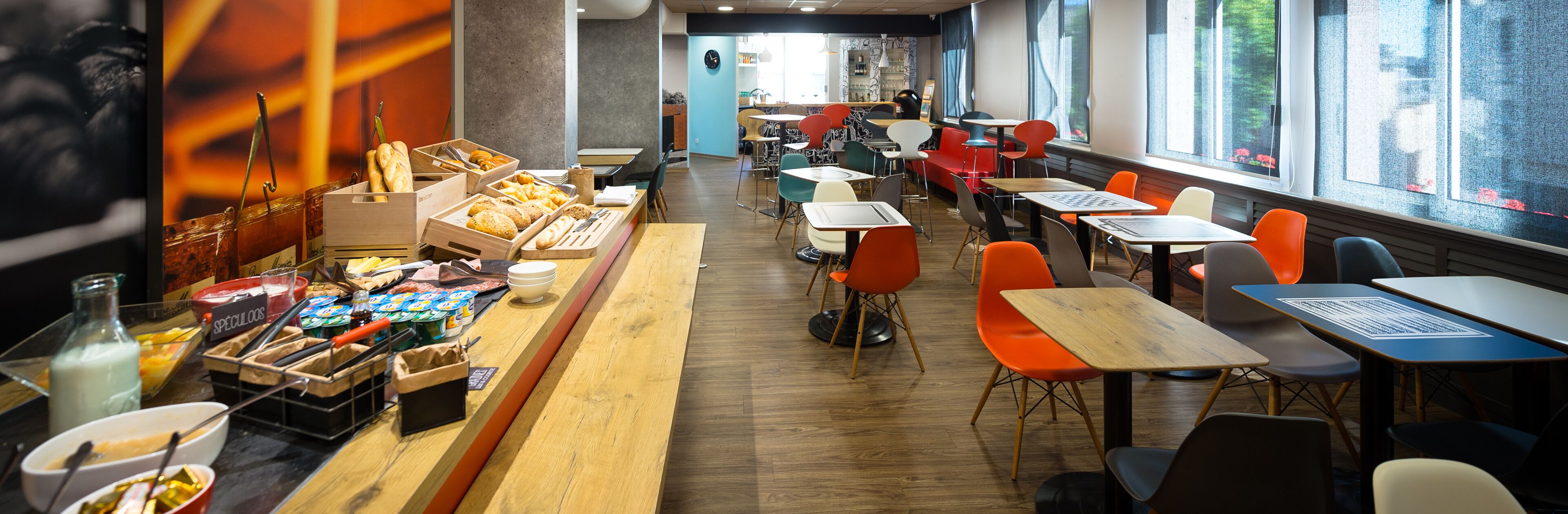 Un café moderno con mesas y sillas de madera, una variedad de productos horneados y una barra de fondo.