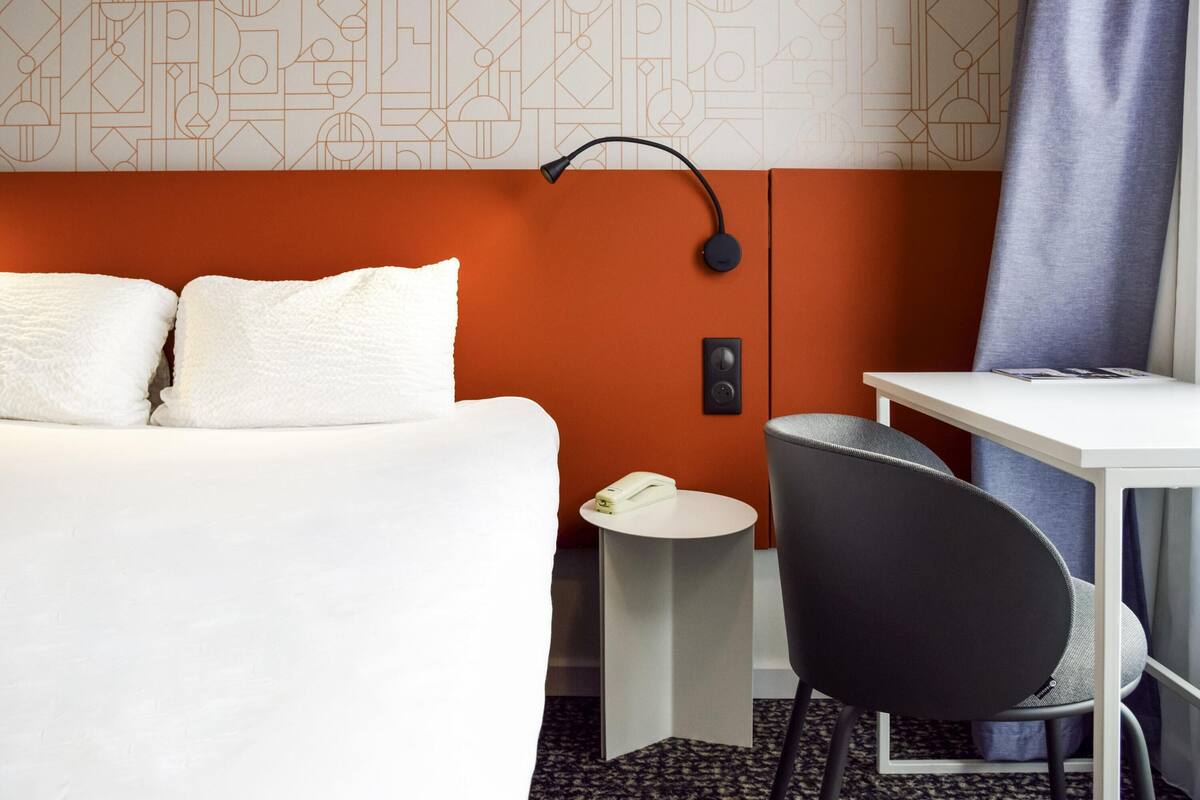 Hotellihuone, jossa on sänky, työpöytä, tuoli, lamppu ja puhelin.