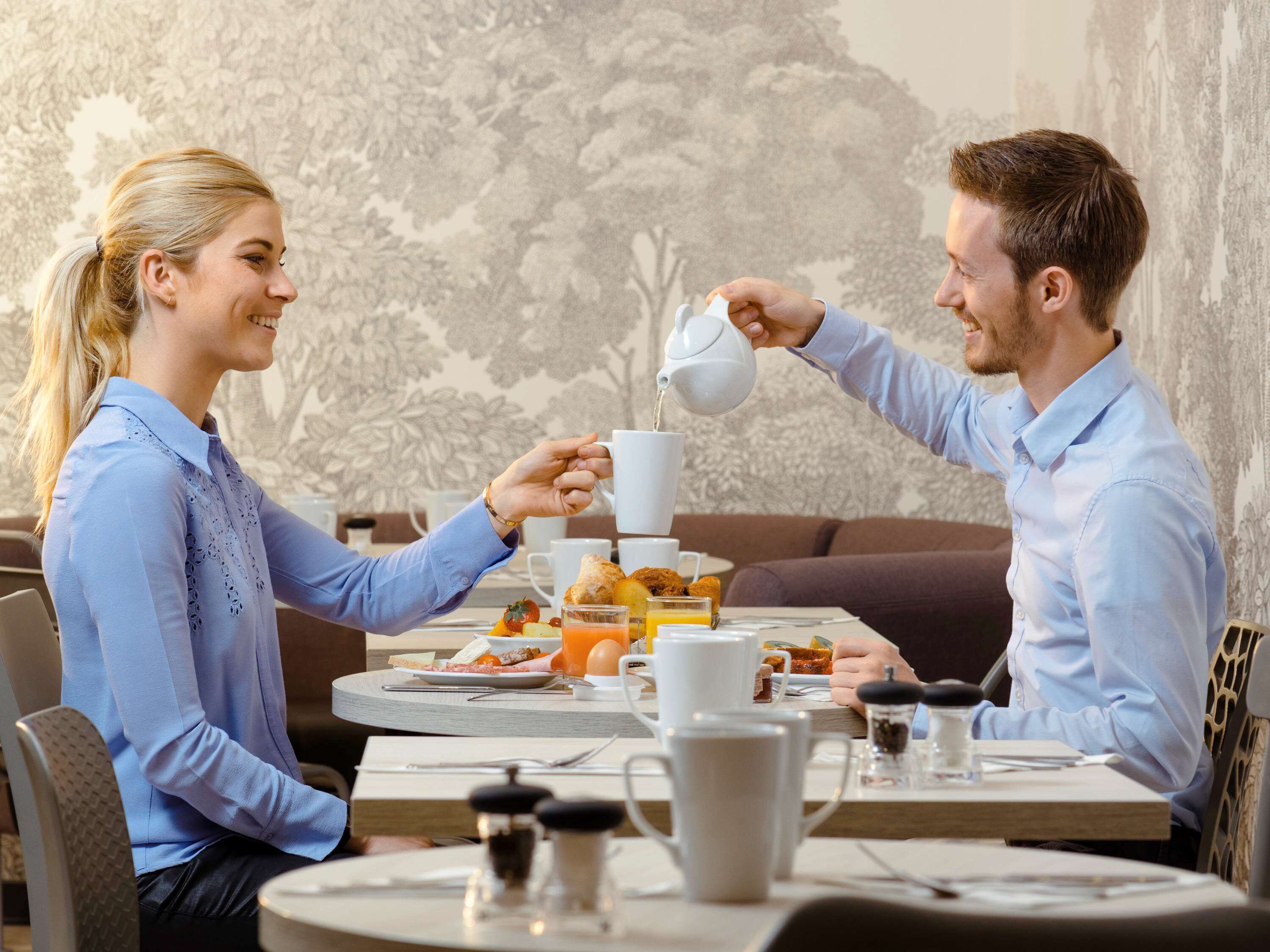 A dining table with breakfast items, a coffee pot, and a cup being poured.