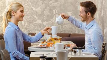 A dining table with breakfast items, a coffee pot, and a cup being poured.
