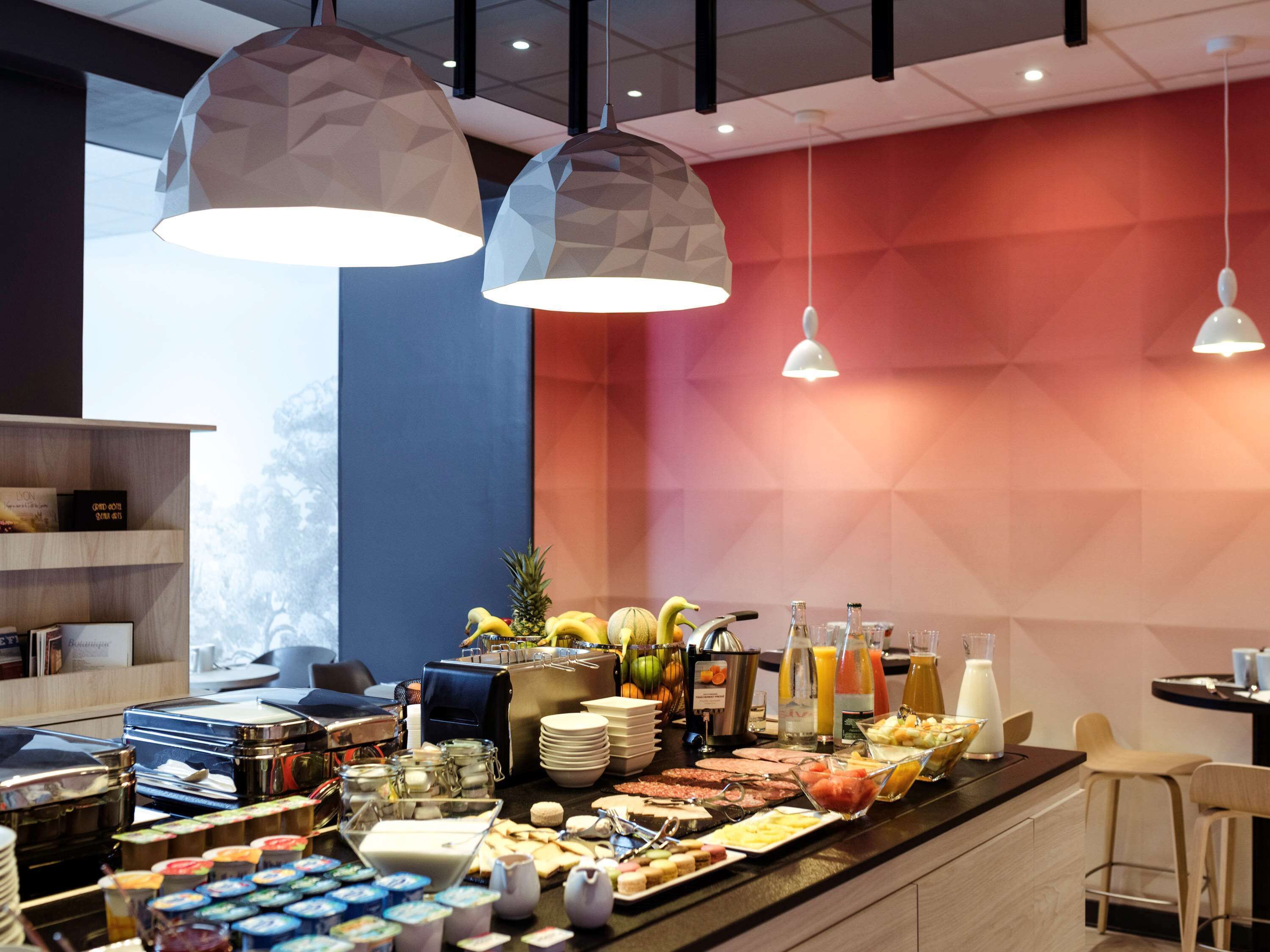 Un bufé de desayuno con diversos alimentos y bebidas, iluminación colgante geométrica y una decoración de interiores moderna.