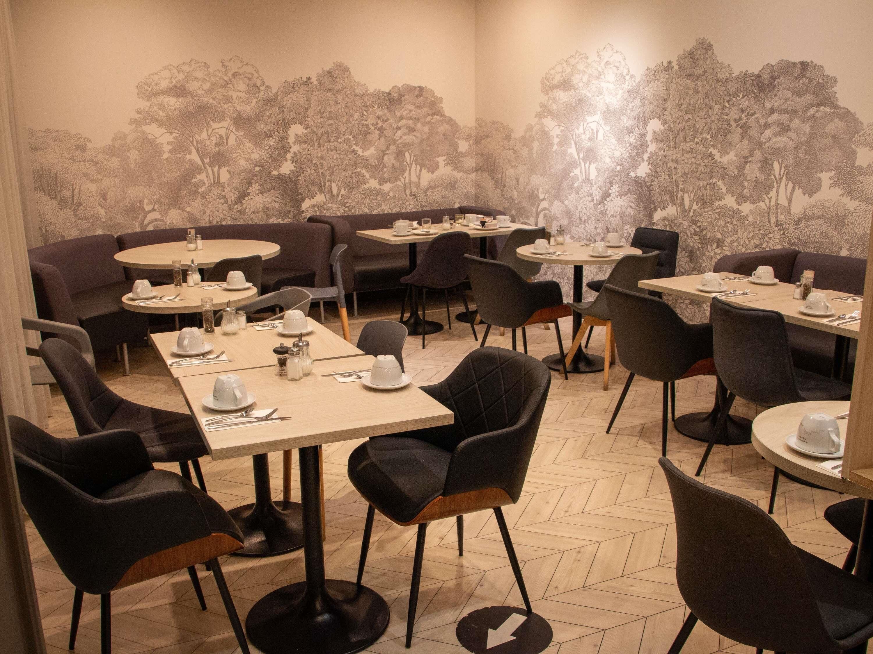 Un restaurante con mesas redondas, sillas negras y un mural de árboles en la pared.