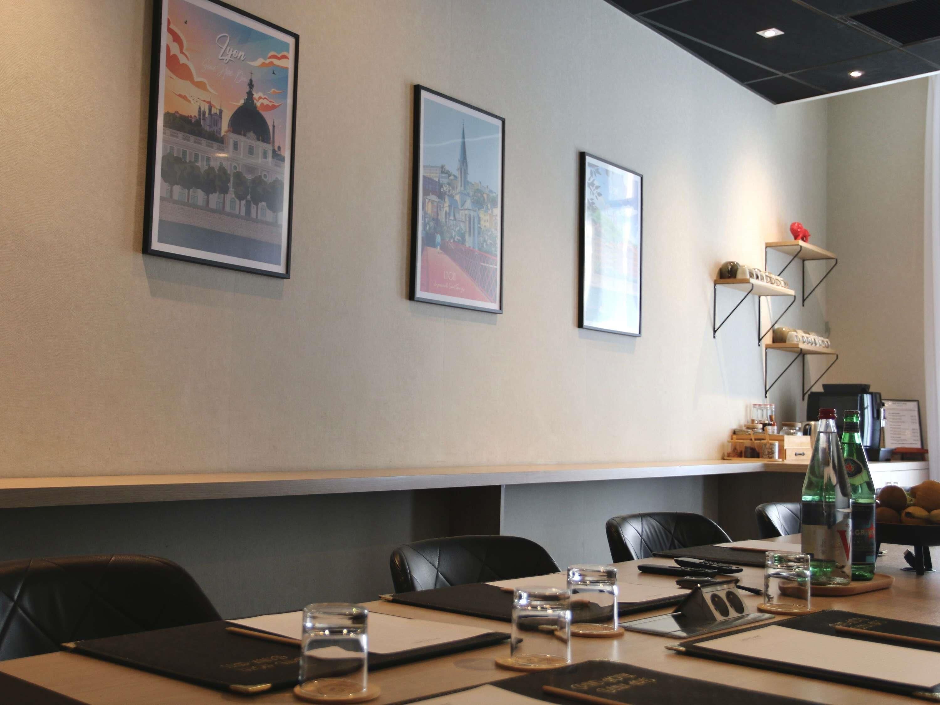 A conference room with a long table, chairs, framed pictures on the wall, and a shelf with items.