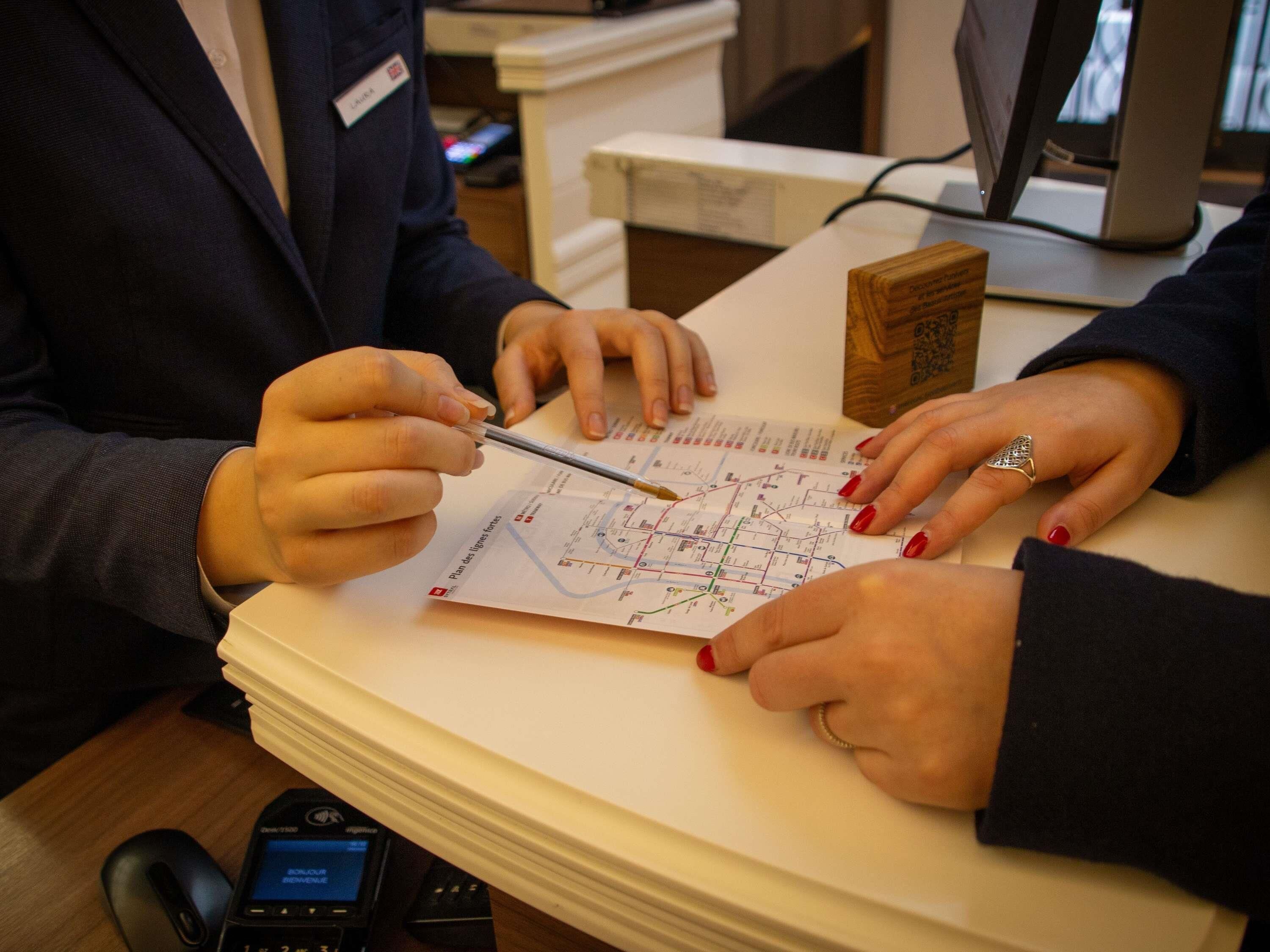 A person holding a pen and a map, another person with a ring, and a computer monitor in a room with a desk and a phone.