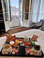 Camera d'albergo con vassoio per la colazione, una tazza di caffè, un teiera e vista sugli edifici dalla finestra.