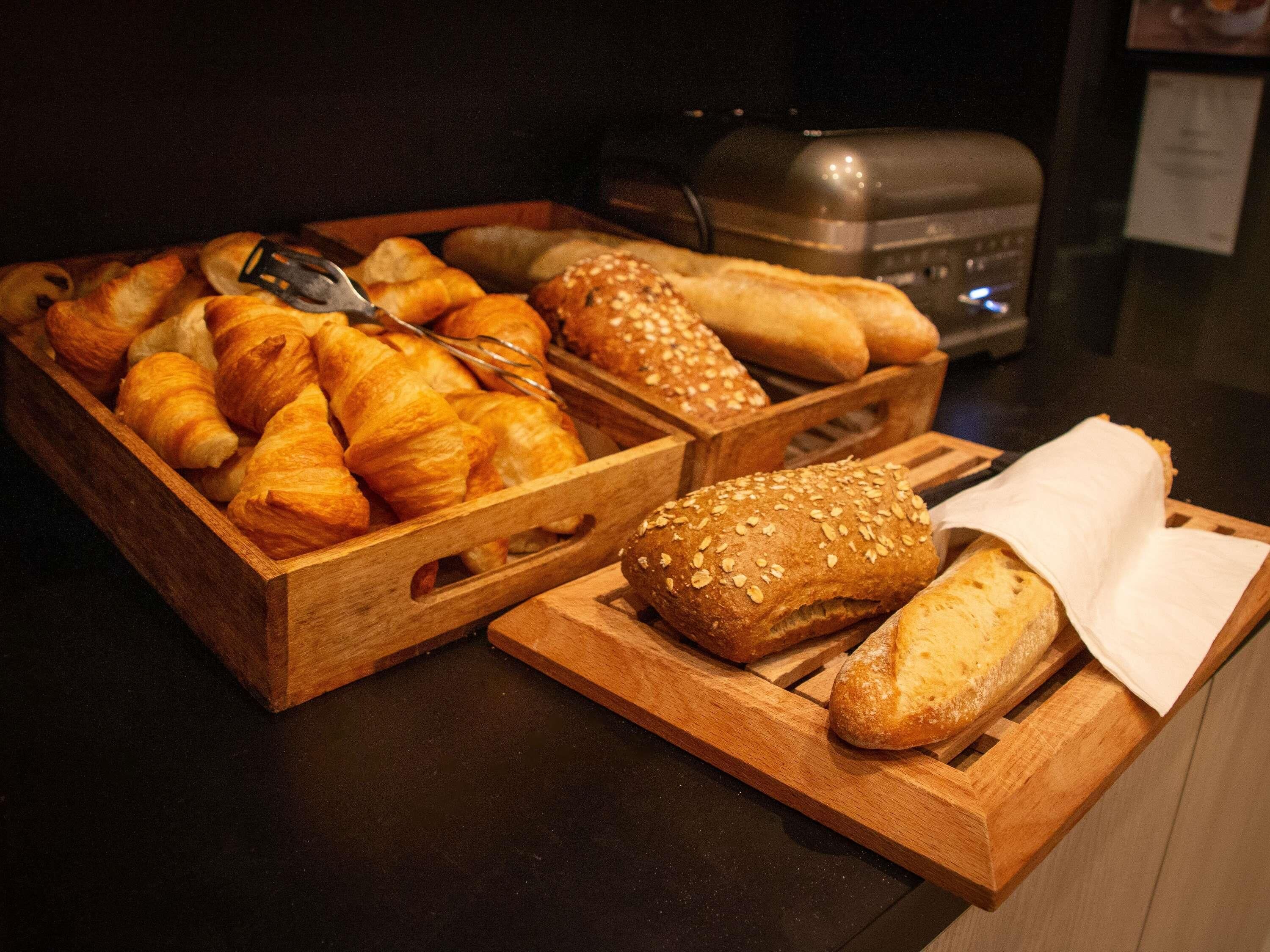 Cesti di legno colmi di prodotti da forno assortiti, tra cui croissant e pane ai semi di sesamo, su un piano di lavoro.