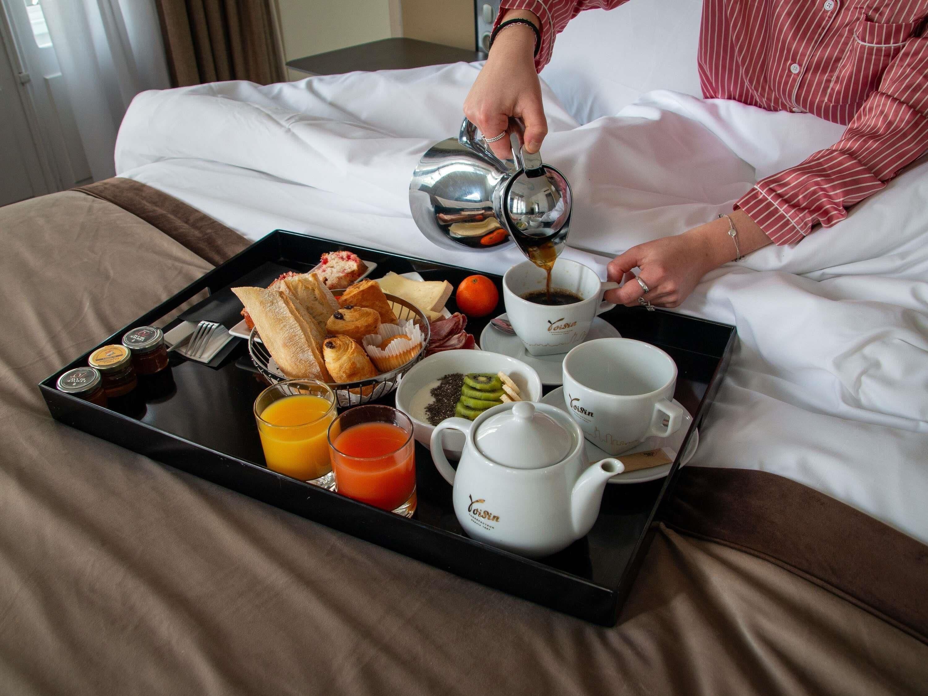 En bakke med morgenmad, indeholdende bagværk, frugt og drikkevarer på et sengebord.