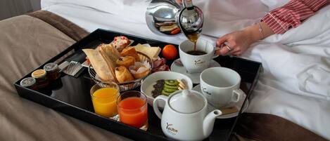 A breakfast tray with pastries, fruits, and beverages on a bed.