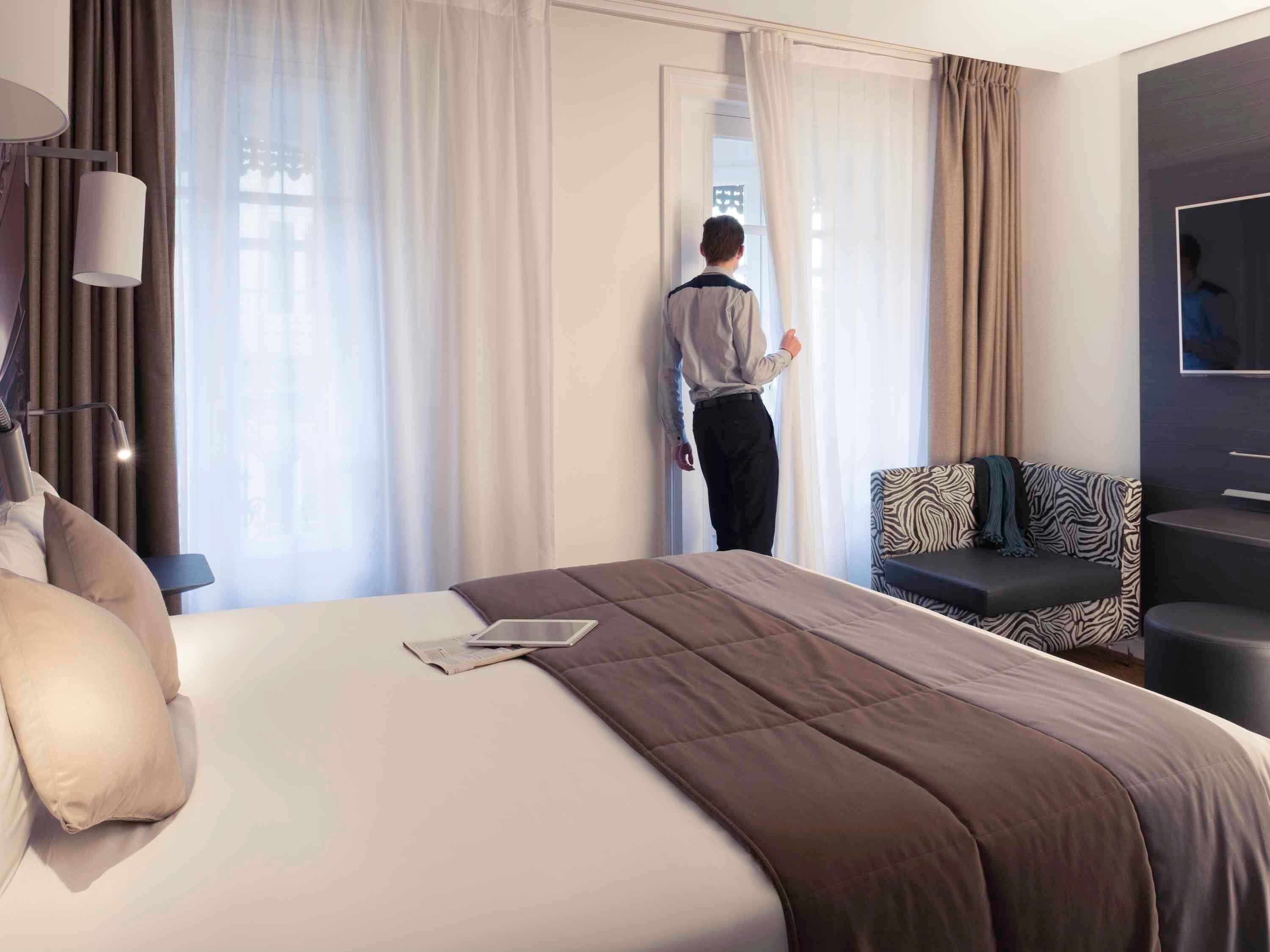 Quarto de hotel com cama, sofá, televisão e janela com cortinas.
