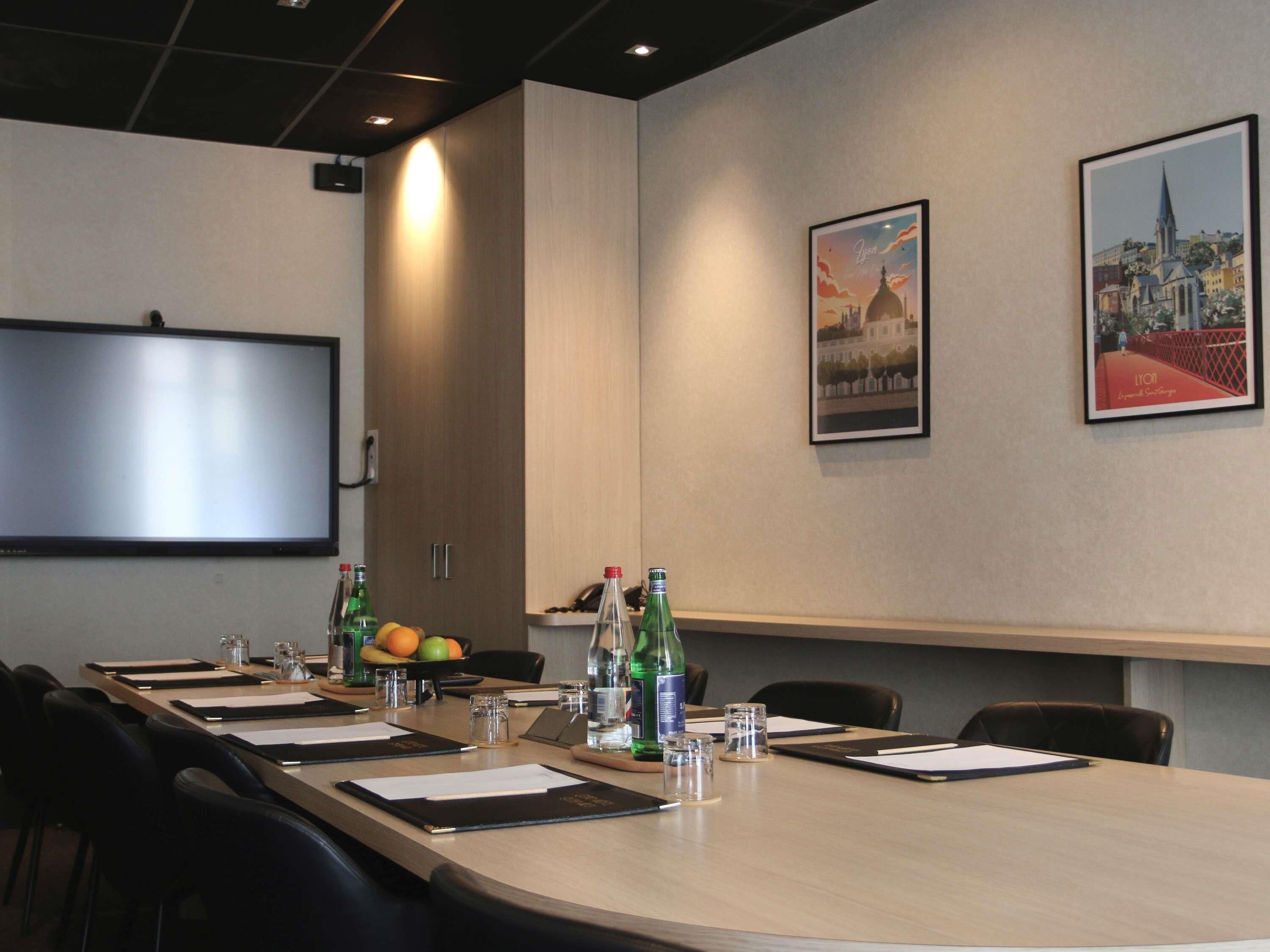 A conference room with a long table, chairs, a projector screen, and framed pictures on the wall.