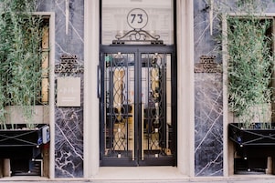 L'ingresso di un hotel con facciata in marmo, il numero '73' sopra la porta e cartelli che indicano 'Grand Hotel Des Deaux Arts'.